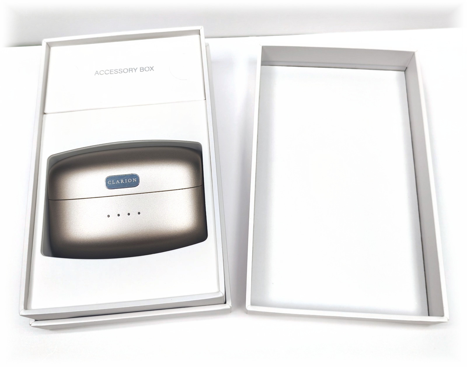 The Clarion presentation box open on white, the charging case seated inside beside the accessory tray.